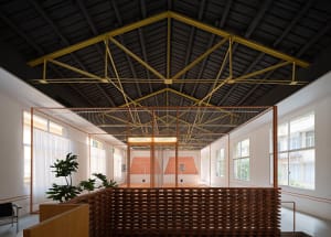 An indoor sports facility with a high ceiling, brick walls, and a grid of metal tubing dividing the space into two courts.