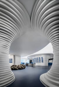 Modern office space with carpeted floor and white columns, featuring a curved ceiling and contemporary design elements.