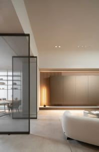 A modern minimalist living room with light-colored flooring, wooden paneling, and a white sofa.