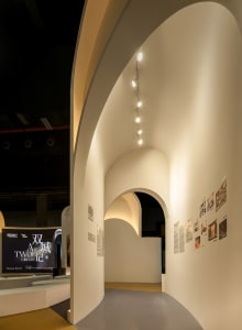 A modern gallery interior featuring white concrete walls and curved arches.