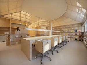 A modern library with minimalist design, featuring wooden desks, fabric-covered shelves, and glass partitions.