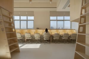A spacious, industrial-style workspace featuring wooden furniture and a long desk with a view of the city.