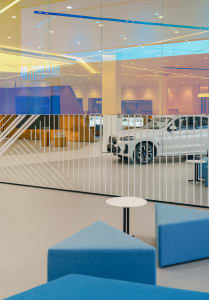 Interior of a modern car dealership with a white car on display behind glass walls.