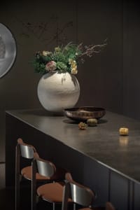 A modern interior decorative arrangement featuring a ceramic vase with a plant bowl and decorative pumpkins.