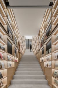 Modern library with stairs and wooden shelves filled with books.