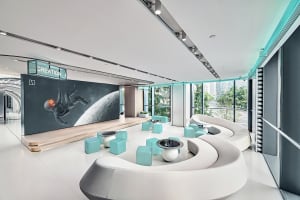 A modern office lounge featuring white and turquoise seating with concrete flooring and concrete seating areas, illuminated b