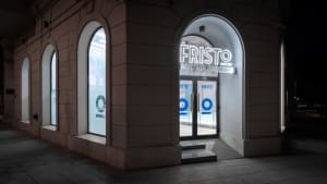 Night view of a storefront with concrete walls and a large arched entrance, illuminated by neon signage.
