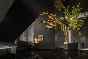 A modern hotel lobby featuring dark metallic cladding and illuminated wood slats.
