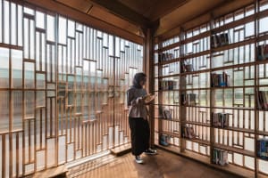 A woman reads a book in a modern library with tall wooden bookshelves.