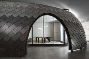 Modern office interior featuring metallic scalloped wall with arched doorway leading to a conference room with sleek design