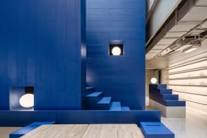 Industrial-style interior design featuring blue walls and stairs with a wooden table and white lamps.