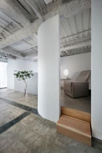 A minimalist living room with concrete floors and walls, featuring a gray recliner and a small potted plant.