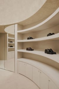 A modern, minimalist shoe closet with concrete shelving and cabinets, showcasing sleek, black leather dress shoes.