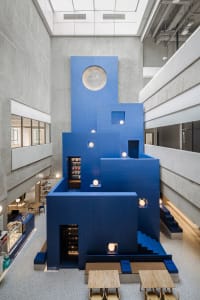 A modern indoor space with blue structures, white lighting, and wooden tables.