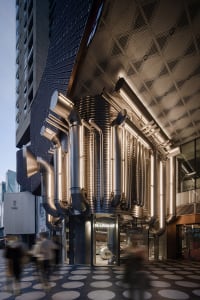 A modern industrial retail storefront featuring large metal pipes on a concrete facade.