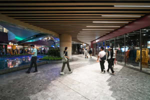 People walking in a modern shopping mall featuring concrete, glass, and tile flooring.
