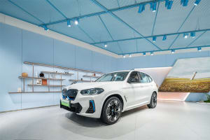 A white BMW SUV with blue accents displayed in a modern showroom with blue ceiling panels.