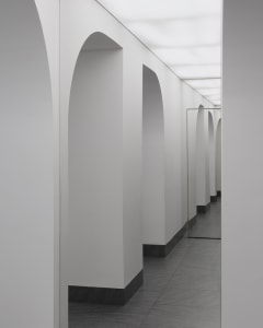 A minimalist corridor with white walls, grey concrete flooring, and arched doorways.