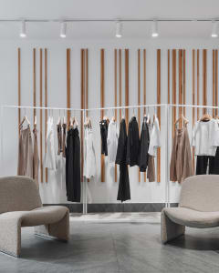 A minimalist clothing store interior with white racks, metallic rails, and wooden backdrop.