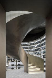 Modern architectural design featuring a spiraling staircase made of metal and glass, with a concrete ground level.