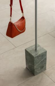An industrial-style marble pedestal holding a red handbag.