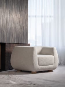 Modern, textured fabric armchair placed in a contemporary living room with a wooden fireplace and white curtains.