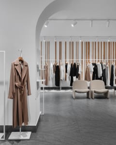 A modern retail store interior with minimalist design, featuring a coat hanging on a white display stand and clothing racks w