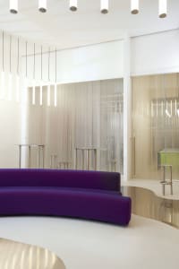 A minimalist office space featuring transparent glass panels, sleek white furniture, and modern lighting fixtures.