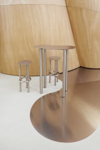 Three modern metal tables with unique curved shapes and stools in a contemporary setting.