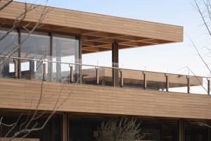 Modern exterior wooden balcony with transparent glass railings.