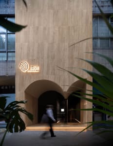 Modern minimalist spa center exterior made of concrete with illuminated signage and green foliage in the foreground.