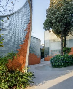 Curved glass and brick facade of a modern urban building with greenery and trees.