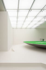 A minimalist white room with a green table and glass ceiling panels.