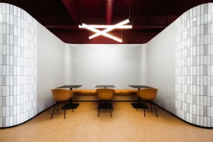 Modern industrial cafe interior with white tiled walls, cork flooring, and orange seating.