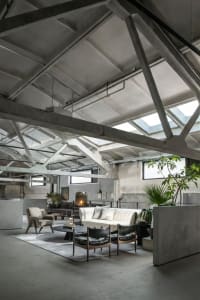 Industrial-style loft living space featuring exposed concrete beams, large windows, and minimalist furniture.
