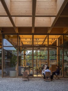 A modern, industrial-style restaurant interior with wooden structural beams and large glass windows.