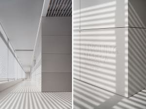 A minimalist corridor with concrete walls featuring textured patterns created by sunlight filtering through vertical windows,