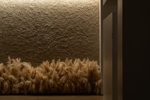 A textured, beige-colored wall adorned with golden-yellow decorative grasses enhancing the ambiance of the space.