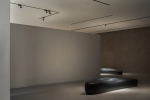 Minimalist modern interior space featuring smooth, textured concrete walls and floors, with contemporary seating and lighting