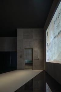 Modern lobby featuring a concrete wall and elevator with a digital display.