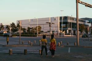 Two people standing on a pedestrian crossing at dusk with a BMW building in the background.