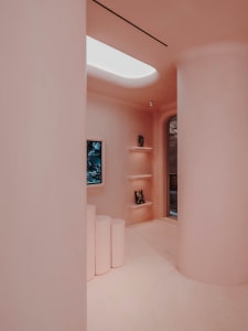 A minimalist interior with pink plaster walls, white cylindrical columns, and a skylight.