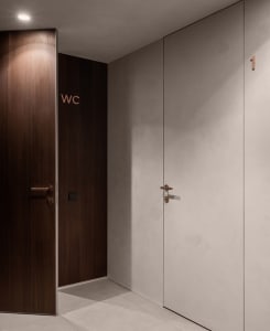 Modern minimalist interior design with a combination of white doors with black handles, concrete walls, and wooden materials.