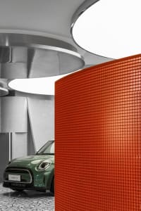 Modern auto dealership showroom with a prominent red panel and a green MINI car on display.