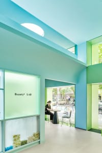 A modern storefront with glass walls and a blue ceiling, featuring a shop window display and seating area.