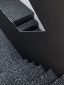 A close-up of a black granite staircase with textured steps and a contrasting wall.