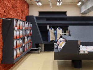 Industrial-style clothing store interior with concrete walls, metal shelves, and glass display cases.