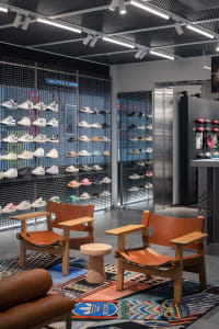 A retail interior featuring a metal grid display wall showcasing various styles of shoes in a store.