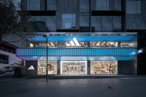 A modern retail storefront featuring glass walls, aluminum accents, and LED lighting at night.