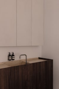 Modern bathroom featuring wooden cabinets, white walls, and a stone countertop with a sink and faucet.